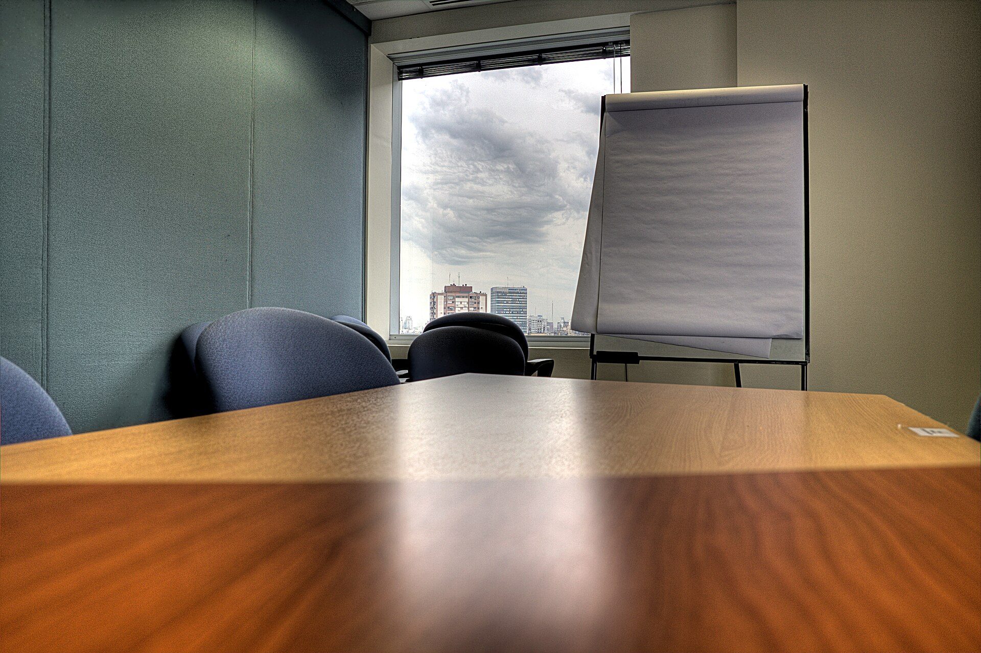 Sala de reunião com mesa longa, cadeiras e quadro de apresentação