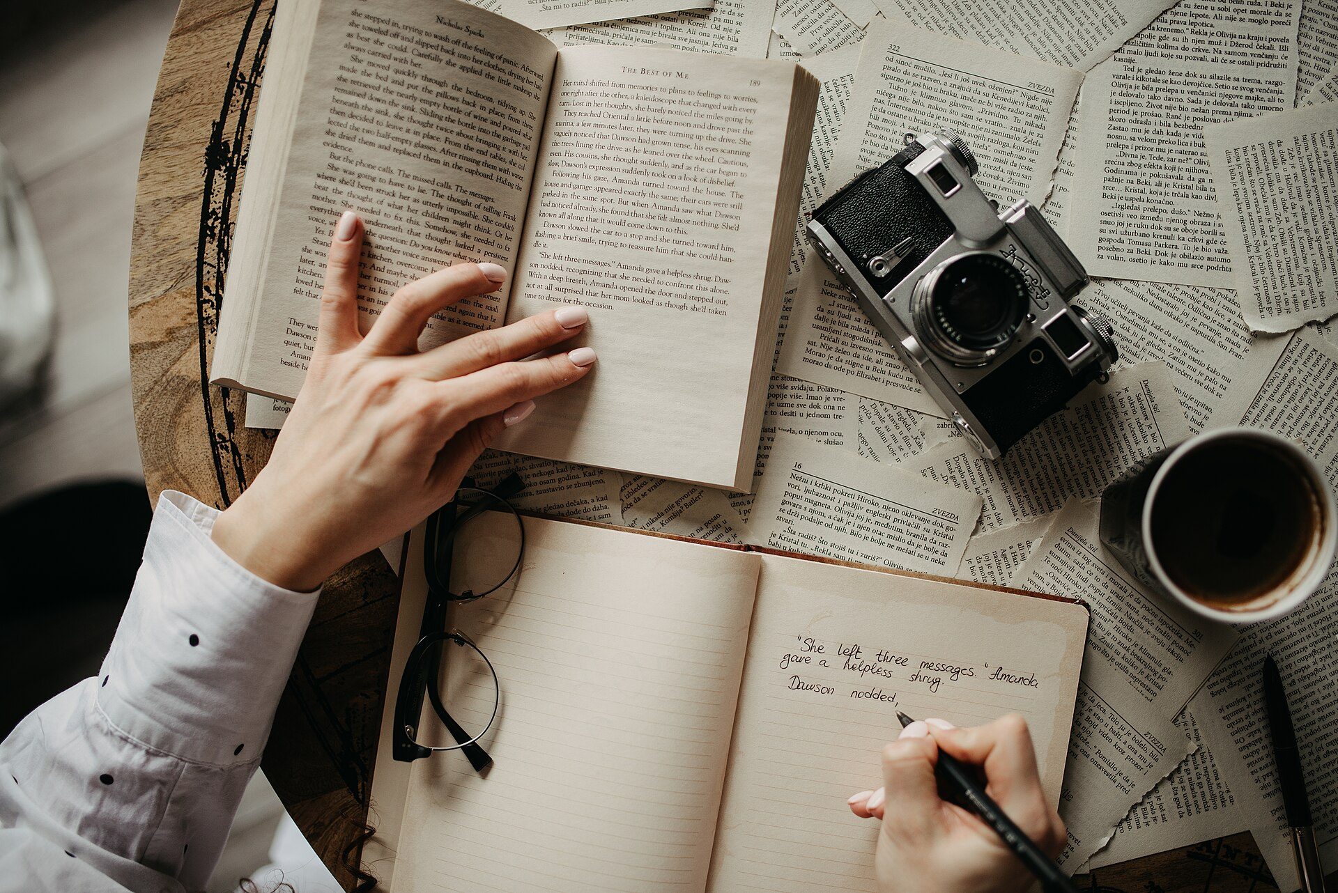 Mãos folheando um livro aberto ao lado de um caderno com anotações