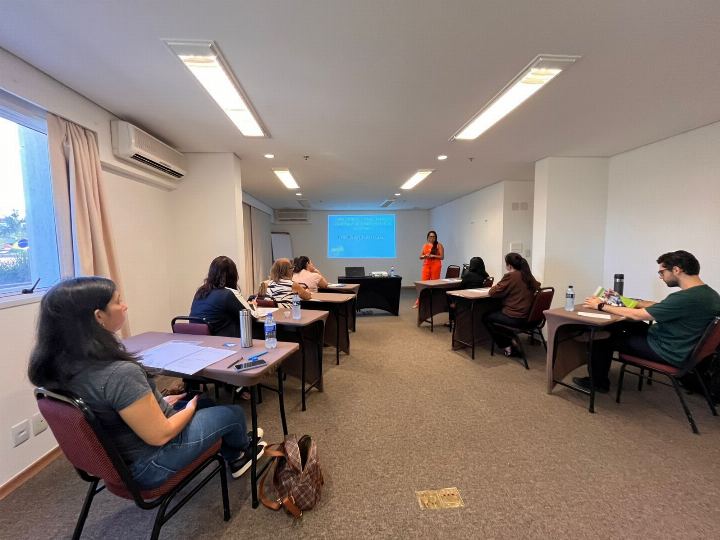 Participantes trabalhando em duplas em sala de treinamento com projeção ao fundo