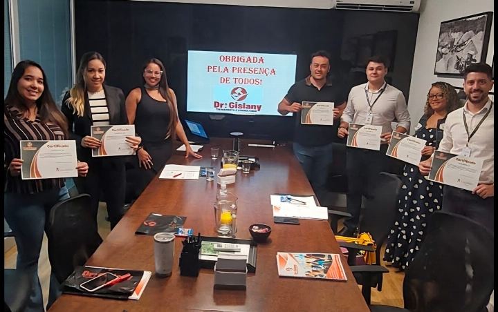 Participantes com os certificados em sala de reunião, diante do slide de encerramento