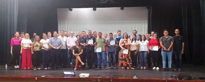 Turma numerosa reunida no palco do auditório com os certificados em mãos