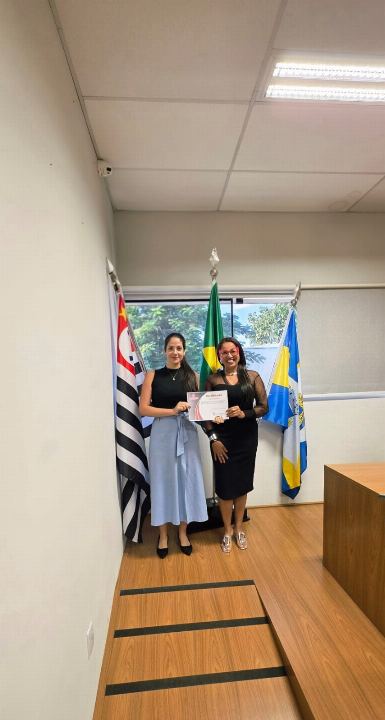 Duas participantes seguram o certificado do curso ao lado das bandeiras do Brasil, de São Paulo e do município