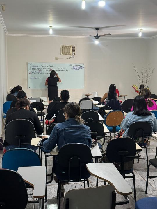 Dra Gislany escreve no quadro branco diante da turma do preparatório para concursos, com alunos sentados em carteiras acompanhando a explicação