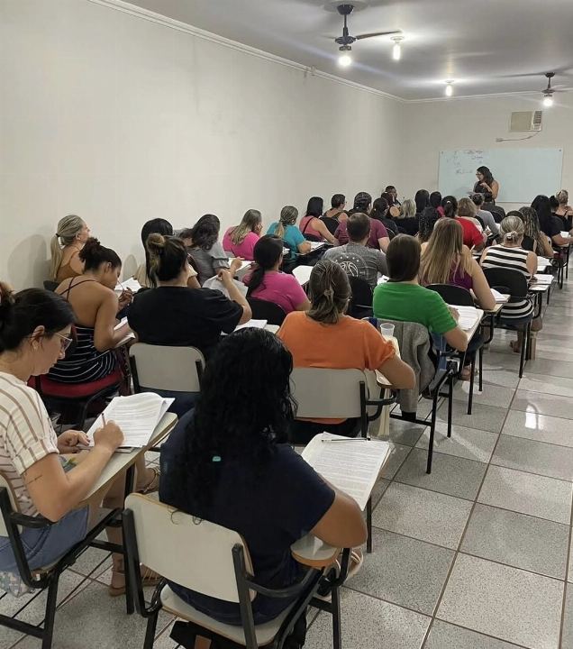 Sala lotada do preparatório para concursos, com alunos resolvendo exercícios nas carteiras e a Dra Gislany ao quadro ao fundo