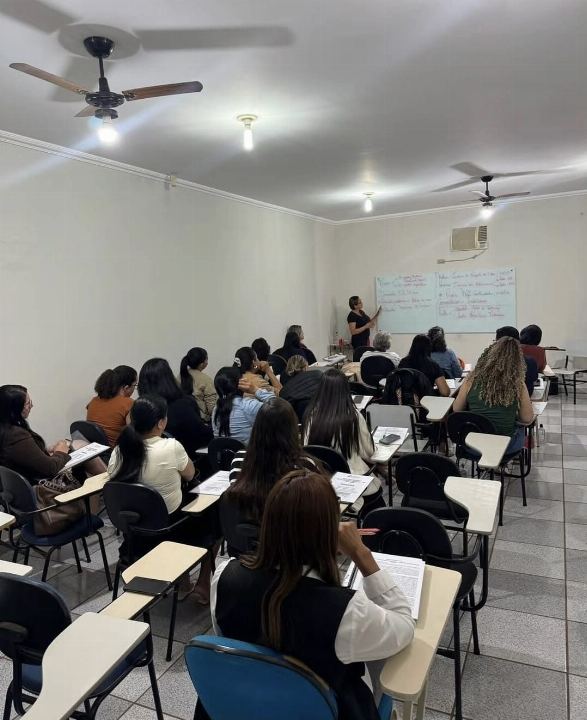 Turma do preparatório para concursos acompanhando a aula e tomando notas, com a Dra Gislany escrevendo no quadro branco ao fundo