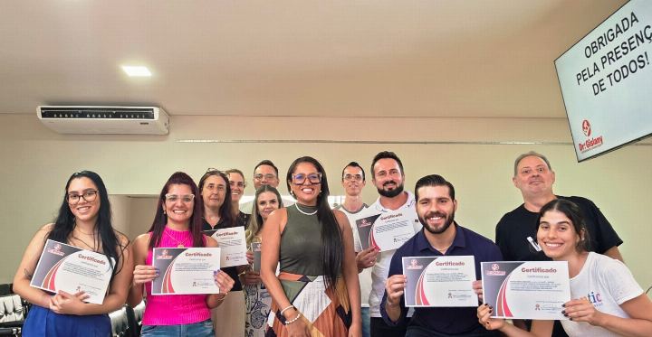 Participantes com os certificados diante do cartaz de encerramento do curso