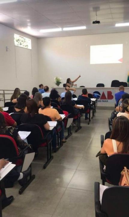 Dra Gislany conduzindo a turma em sala de aula com carteiras ocupadas