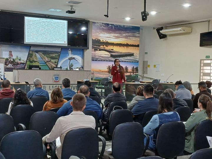 Plenário de câmara municipal lotado de servidores durante treinamento, com a Dra Gislany ao microfone à frente da mesa diretora