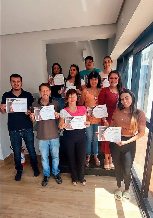 Turma com os certificados em sala iluminada por janela ampla