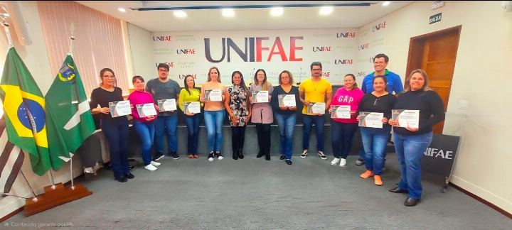 Turma com os certificados diante do painel institucional do UNIFAE