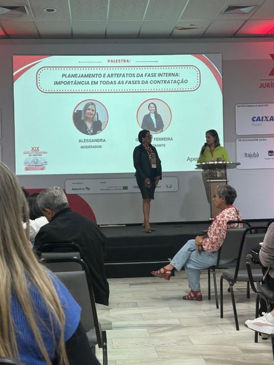 Dra Gislany ao lado de outra palestrante durante apresentação sobre planejamento e artefatos da fase interna da contratação, diante de plateia em evento