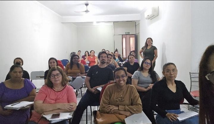 Alunos do preparatório para concursos sorrindo para a foto, sentados nas carteiras com apostilas e cadernos abertos