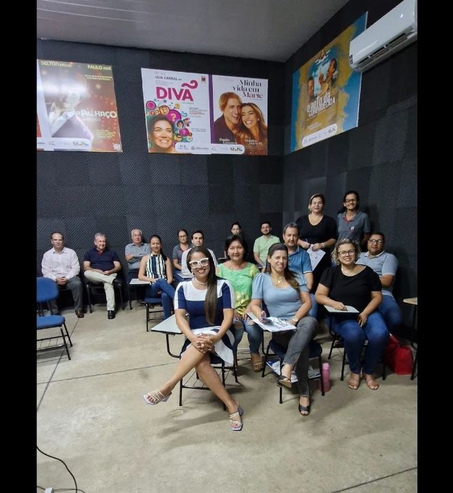 Turma reunida em sala de treinamento com banners do evento ao fundo