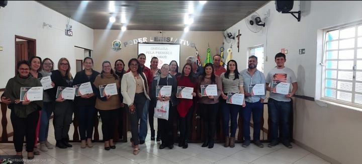 Turma com os certificados em sala institucional com bandeiras ao fundo
