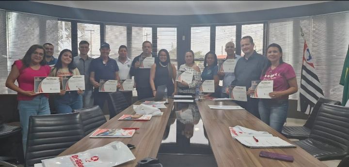 Participantes com os certificados em torno da mesa de reuniões, com a bandeira de São Paulo ao fundo
