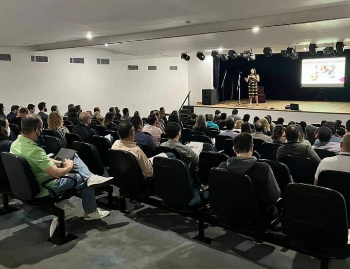Auditório grande com plateia numerosa durante a palestra, com a apresentação projetada no telão