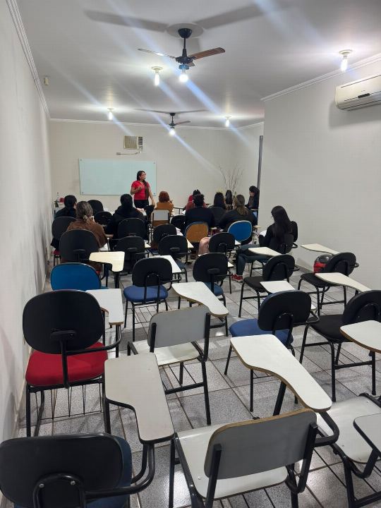 Sala de aula do preparatório para concursos vista do fundo, com a Dra Gislany ao lado do quadro branco e os alunos nas carteiras