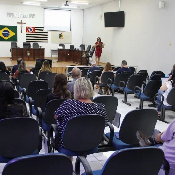 Sala de sessões com plateia atenta e a Dra Gislany conduzindo o treinamento à frente