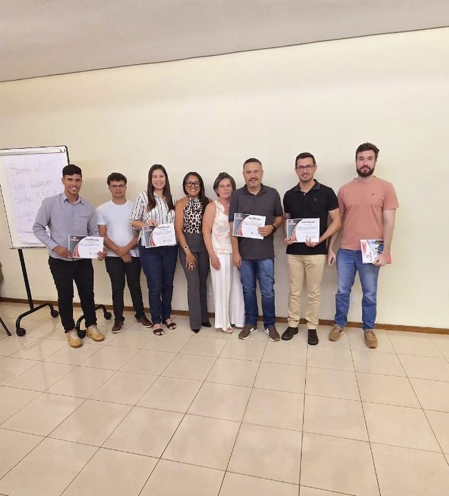 Participantes com os certificados em sala clara, ao lado do quadro do treinamento