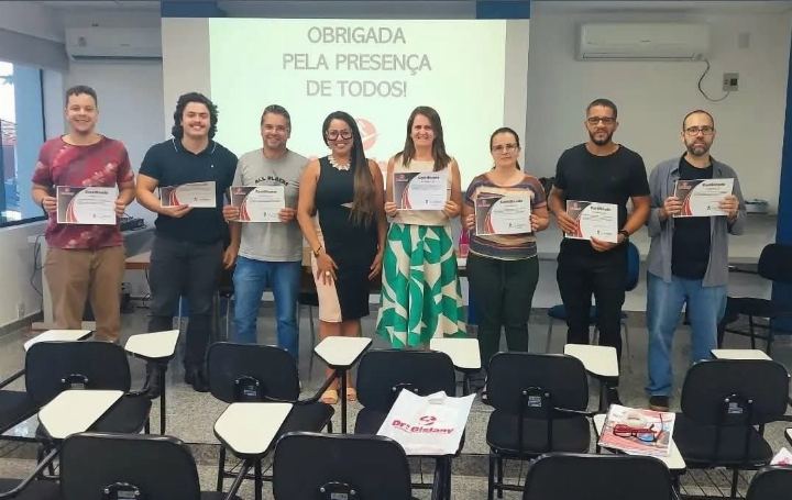 Turma com os certificados em sala de aula, diante do slide de agradecimento